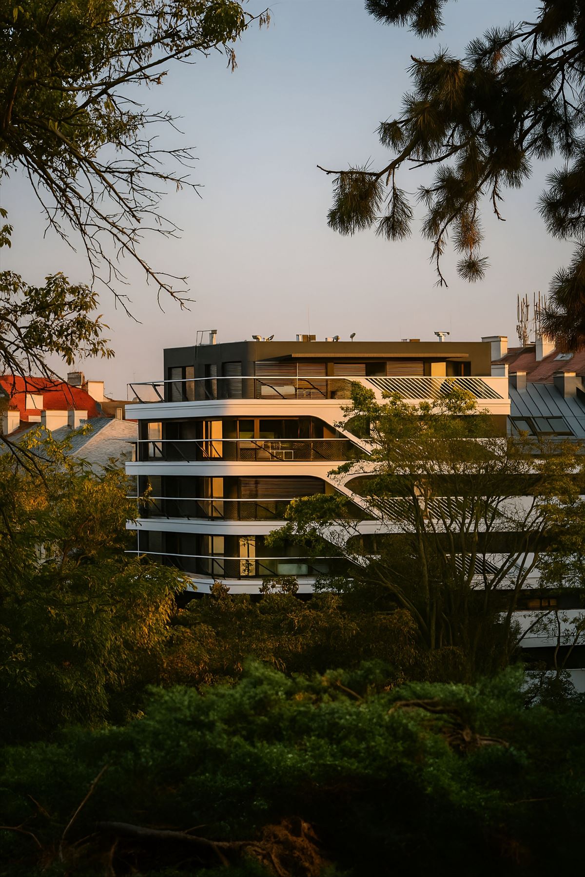Edificio residencial de baja altura entre árboles, con luz de tarde
